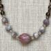 Front view of a beaded necklace in shades of purple. A center bead is made from a shell.